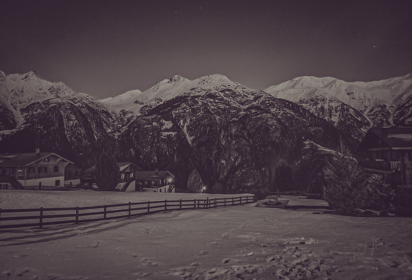 A breathtaking monochrome view of a snow-covered village in Zermatt, Switzerland, nestled beneath towering alpine mountains under the night sky.