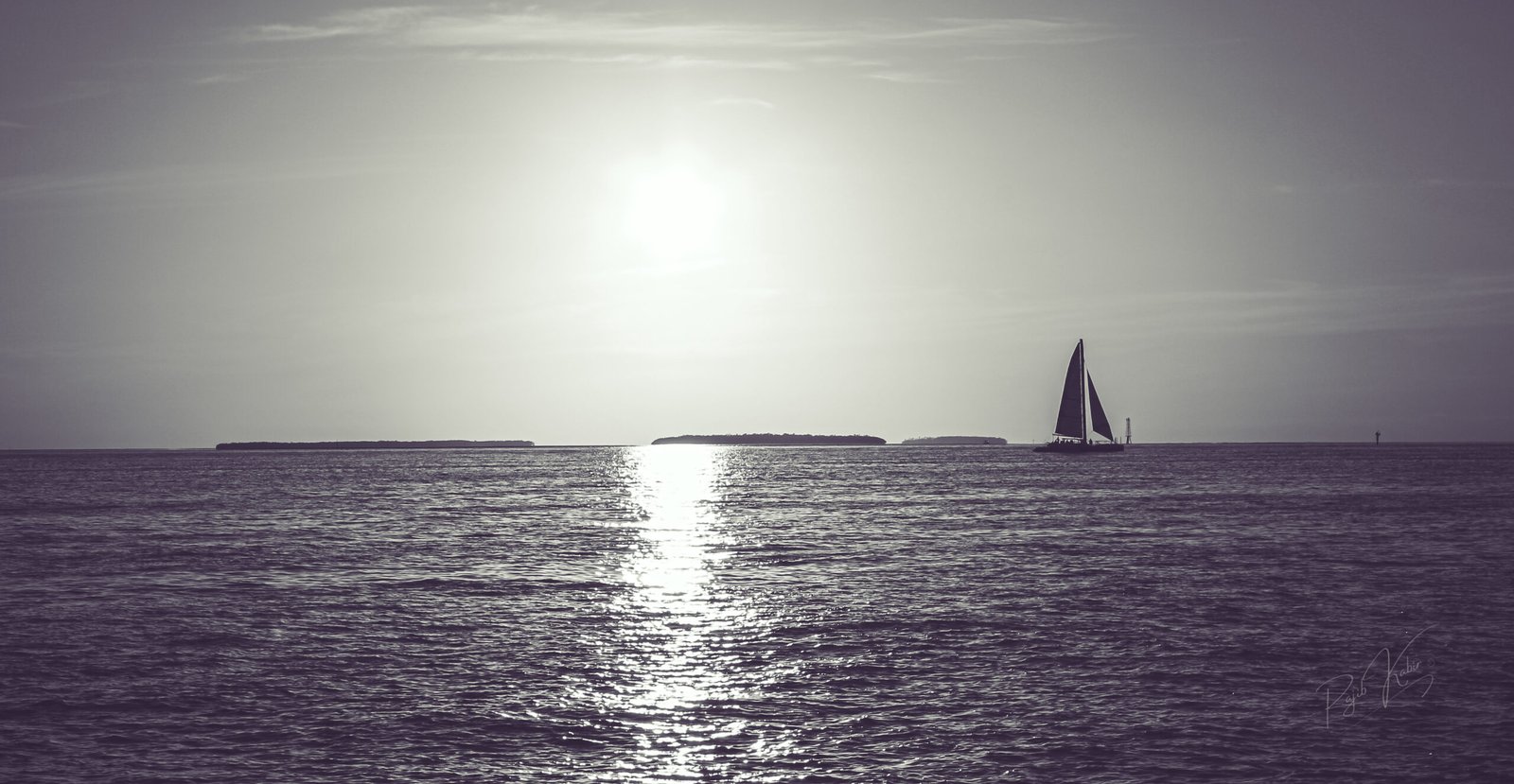 A sailboat gliding through a calm ocean at sunset, with golden reflections on the water.