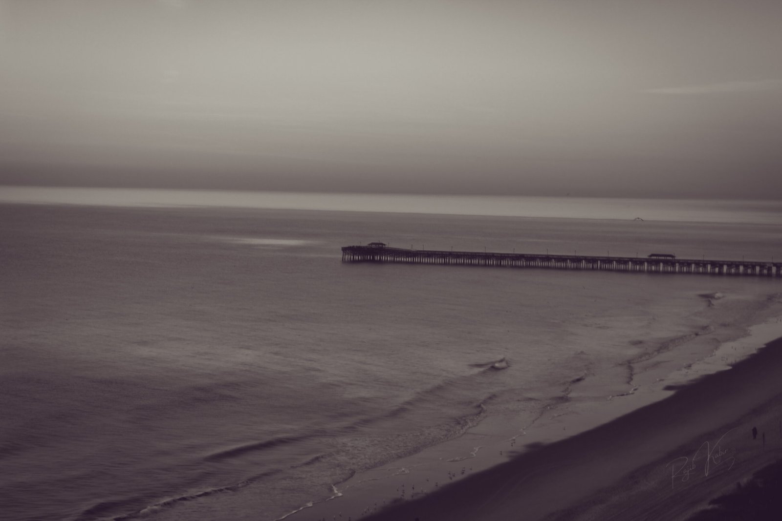 A quiet ocean horizon with a wooden pier extending into the distance.