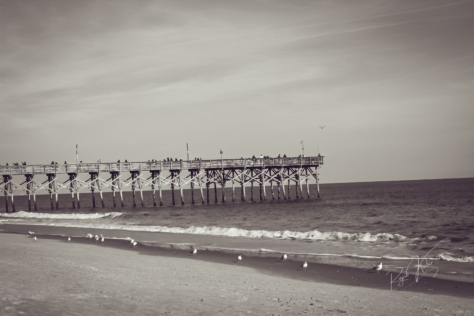A peaceful wooden pier extending into the ocean at sunrise, captured by Rajib Kabir.