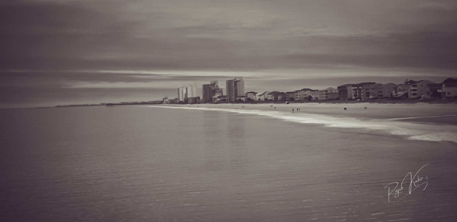 A panoramic view of the city skyline along a peaceful coastal beach at dusk.