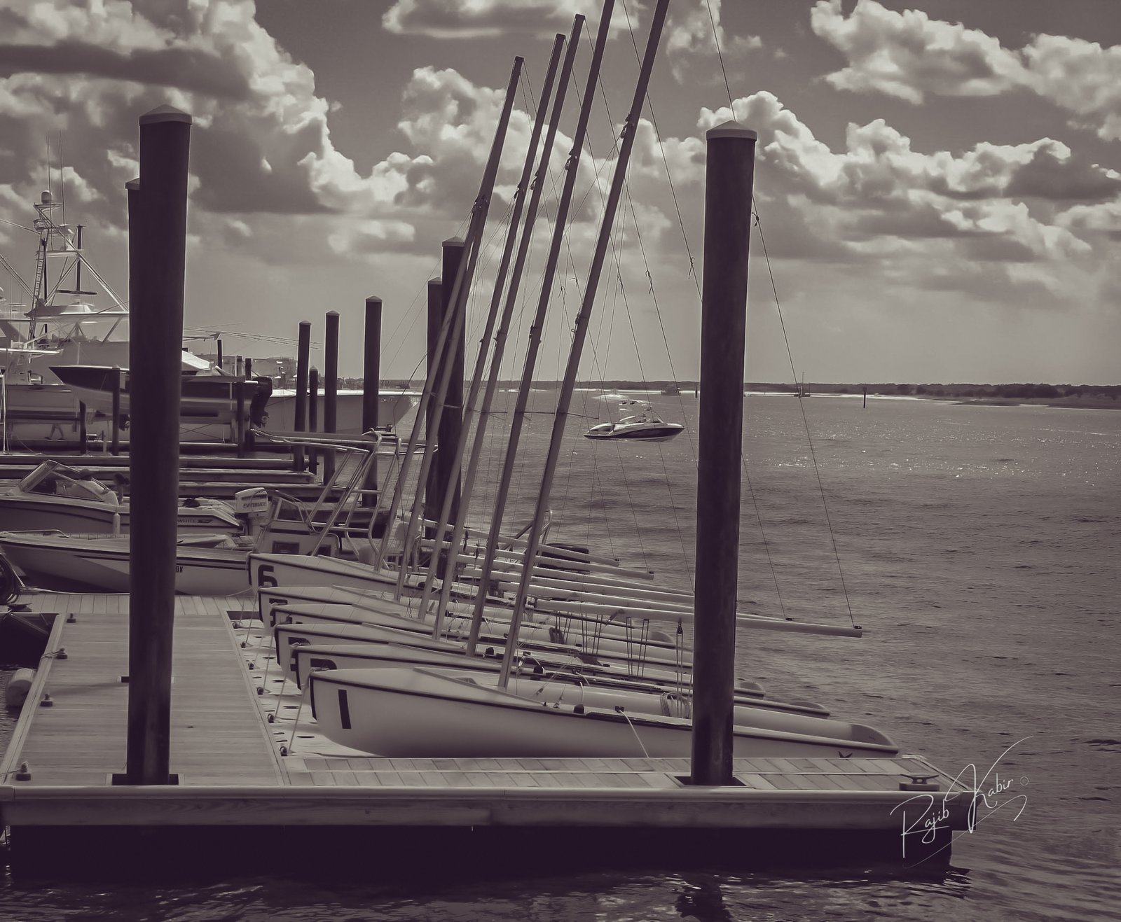 A peaceful black-and-white image of a wooden dock extending into calm waters, captured by Rajib Kabir
