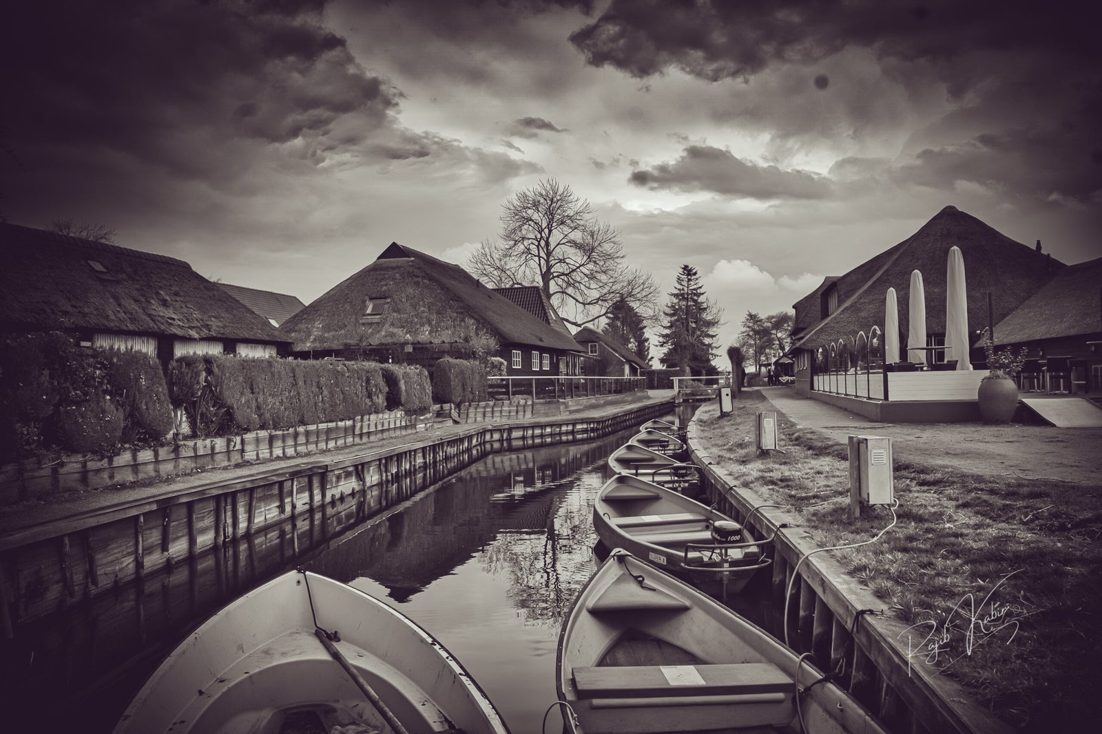 A monochrome view of the iconic Amsterdam canals, featuring charming houseboats and historic Dutch architecture under a dramatic sky.